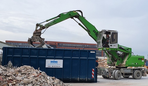 Bagger lädt Bauschutt in großen Container auf Baustelle für Entsorgung und Recycling.