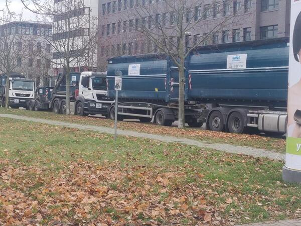 Mehrere Lkw mit Containern parken im Herbst vor einem Bürogebäude in der Stadt.